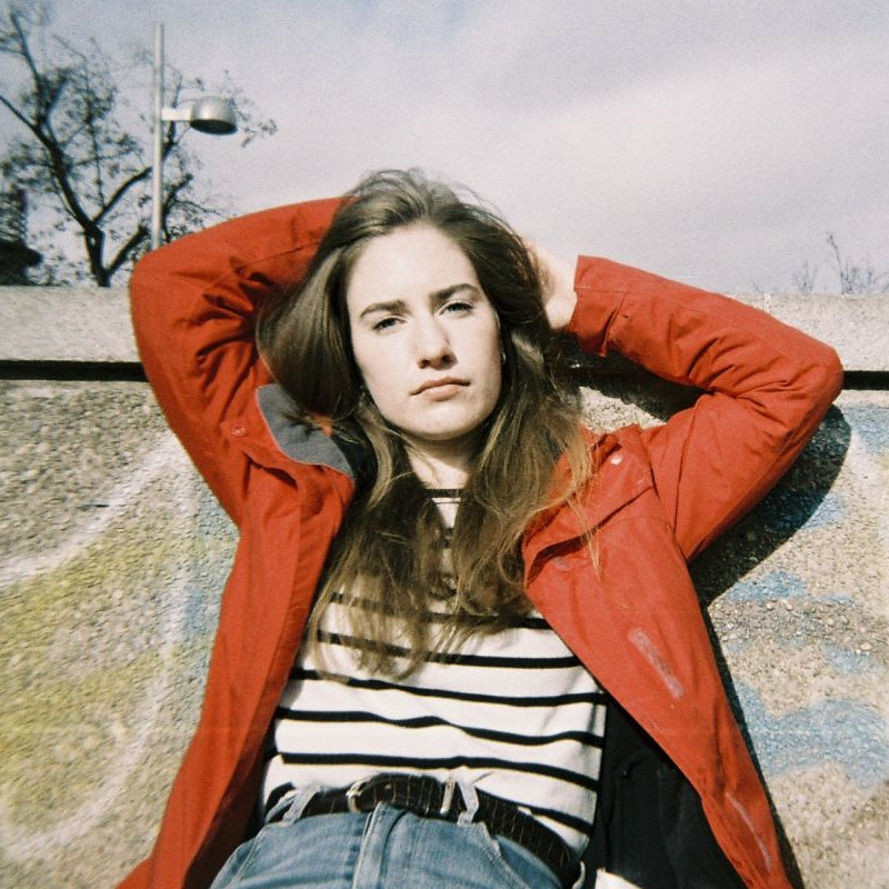 Person wearing a red jacket and striped shirt leaning against a wall with graffiti.