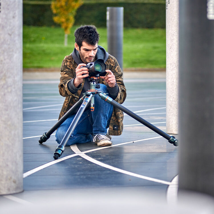 Man with a tripod spread out in an area with large columns and grass