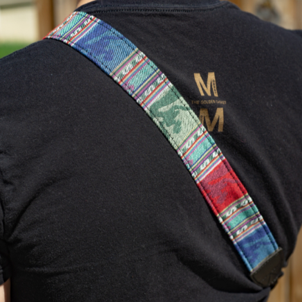 A camera strap with a multicolored pattern and black leather ends.