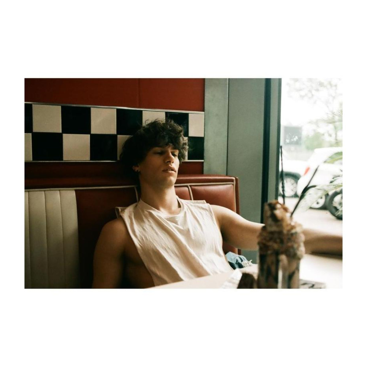 Young man sitting in a retro diner booth with red and white upholstery, captured with vintage analog film aesthetics.