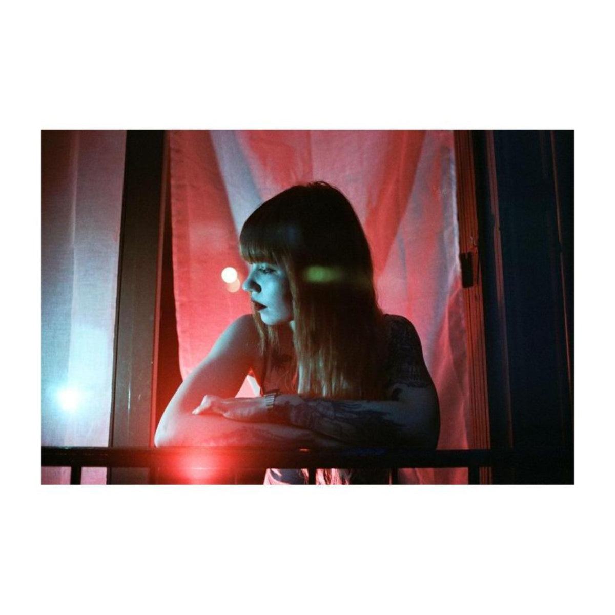 Woman leaning on a balcony at night, captured with vibrant red and purple color shifts characteristic of LomoChrome film.