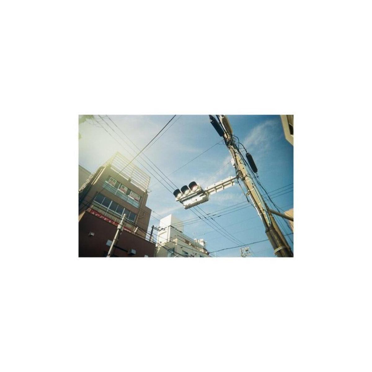 Panoramic shot of a city street with buildings, power lines, and traffic lights against a bright blue sky.