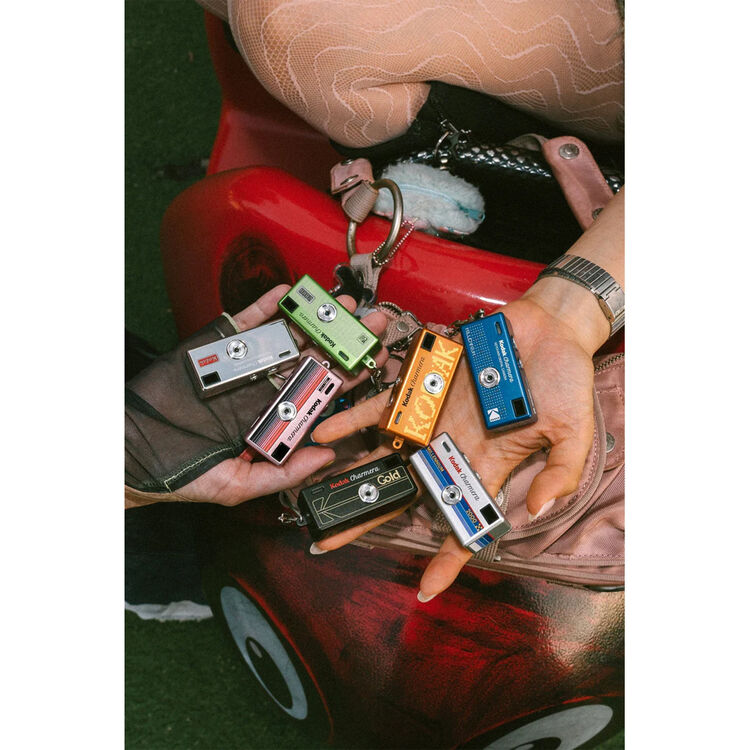 Collection of vintage cassette tape keychains held in hands with a red car in the background.