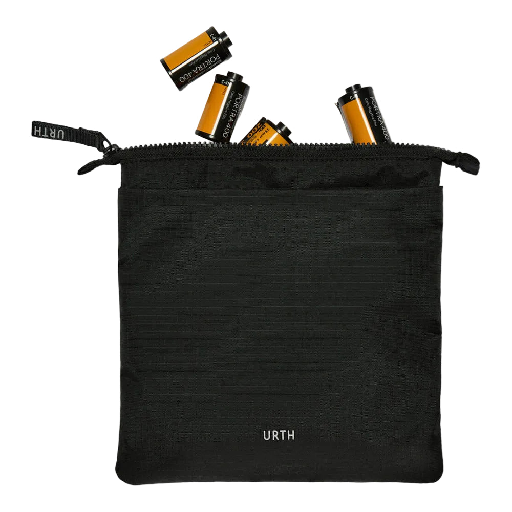 A black zippered pouch with the URTH logo printed in white near the bottom, shown on a white background with several film canisters spilling out from the top.