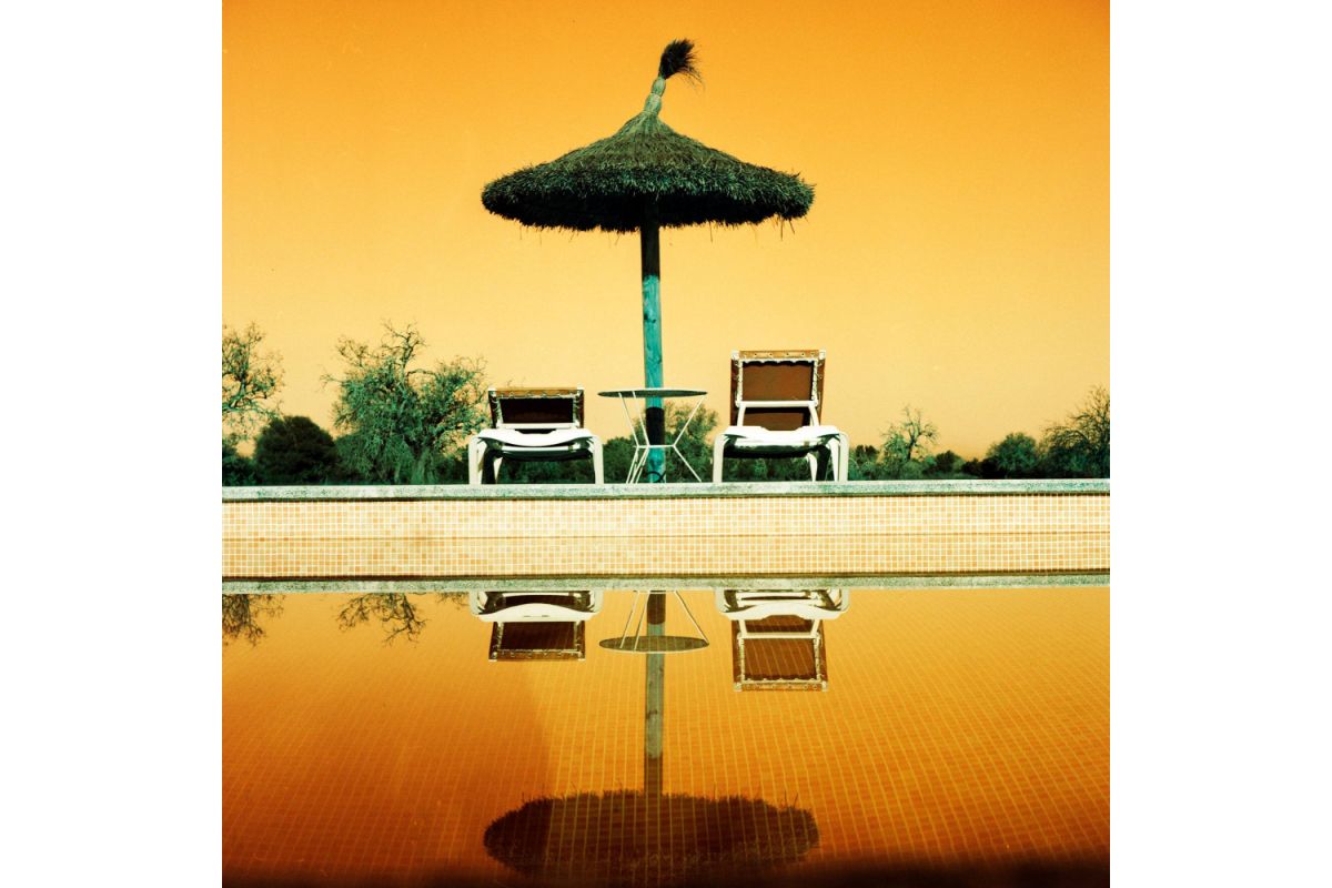 Poolside setting with a thatched umbrella and chairs on a yellow-orange gradient background