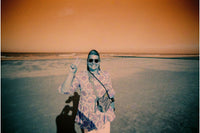 Person in a patterned shirt and sunglasses standing on a salt flat with an orange sky.