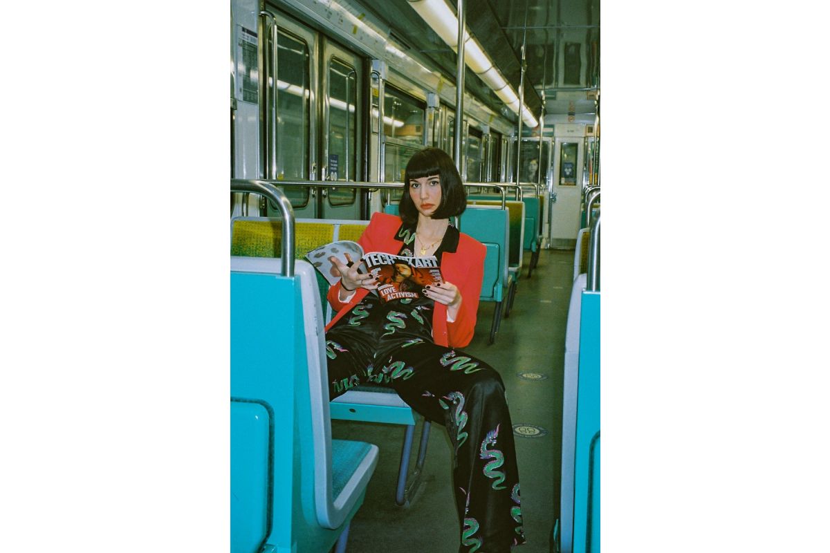 Person sitting on a train holding a dog, wearing a black outfit with green patterns.