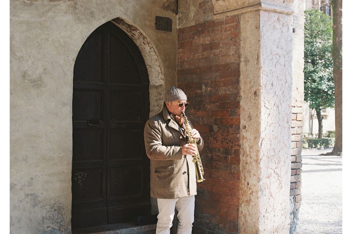 Person playing a saxophone against a stone building with an arched door.