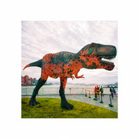 Dinosaur statue with floral pattern in front of a waterfront with people watching