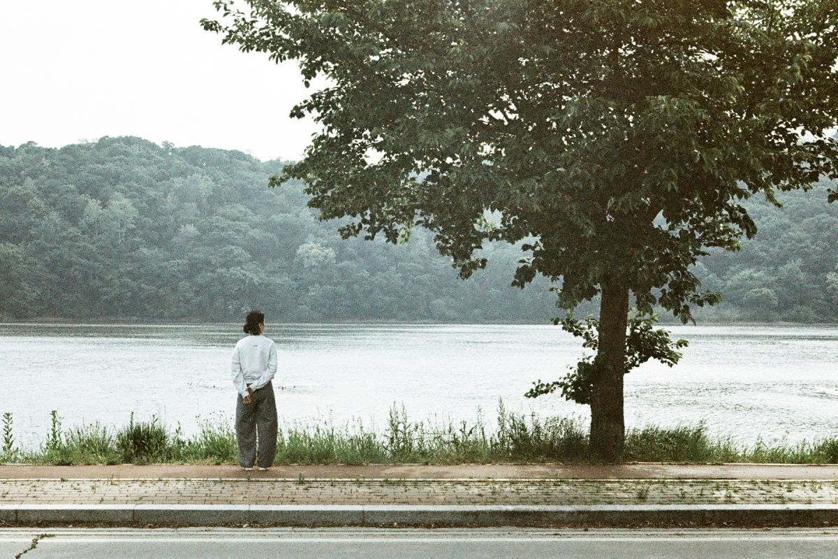 Person standing by a lake with trees and mountains in the background