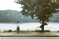 Person standing by a lake with trees and mountains in the background