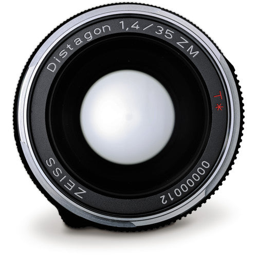 A close-up studio shot of a Zeiss Distagon 1.4/35 ZM lens, showing the front glass element, black and silver metal barrel, and white engraved text on a clean white background.