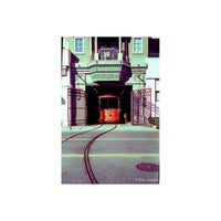 A vintage red cable car emerges from a dark tunnel beneath a green building, with curved tracks in the foreground and open metal gates on both sides.