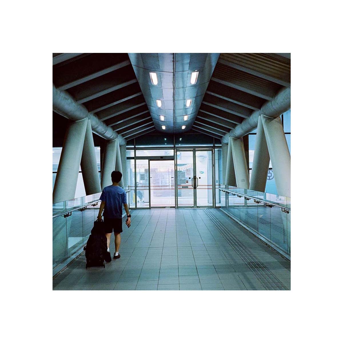 Person walking through a modern, tungsten-lit pedestrian bridge, captured on Amber AHU T640 35mm color film.