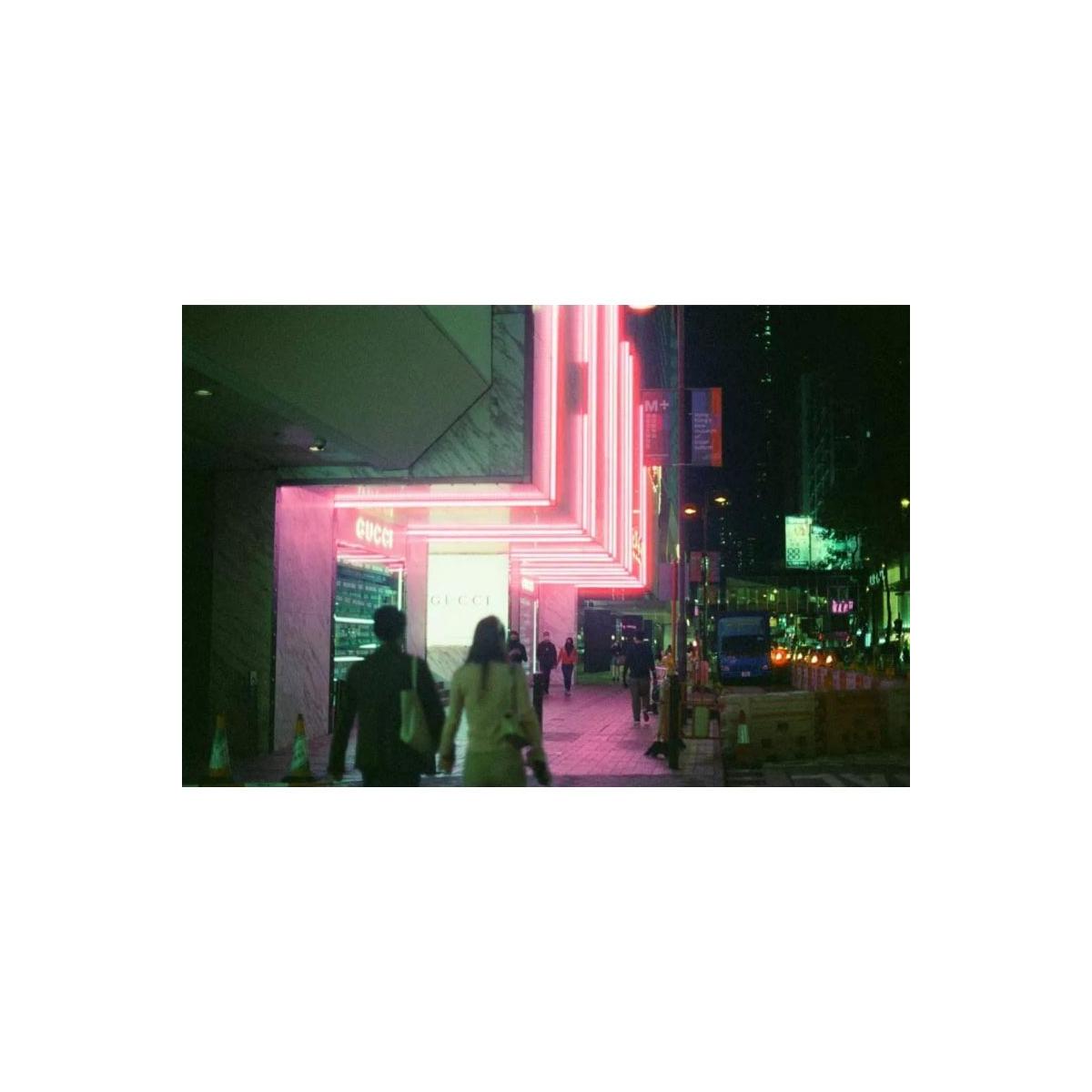 A nighttime street scene featuring a brightly lit Gucci storefront with pink and white neon-like lighting, with pedestrians walking in front of the entrance.