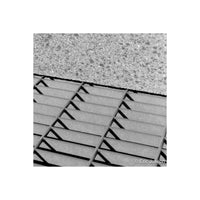 Black and white close-up photograph of textured concrete or stone tiles meeting a slatted metal grate, with a photographer's copyright watermark in the bottom right corner.