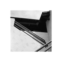 Black and white architectural photograph of an outdoor staircase with dark metal railings against a textured white wall and dark roofline.