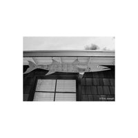 A large fish-shaped metal wall hanging with a spotted pattern, mounted under the eaves of a house above a window.