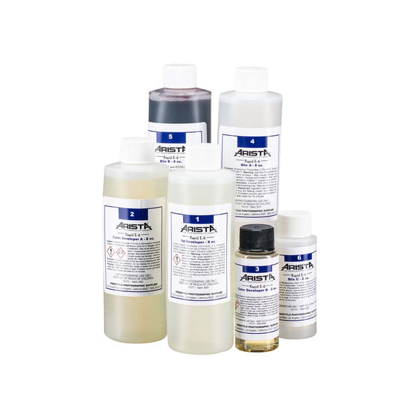 Arista Rapid E-6 slide film developing kit with six labeled plastic bottles of chemical solutions on a white background.