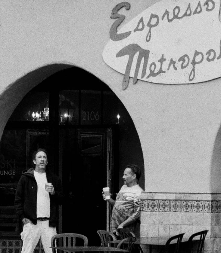 Black and white image of Espresso shop with two men holding paper coffee cups.