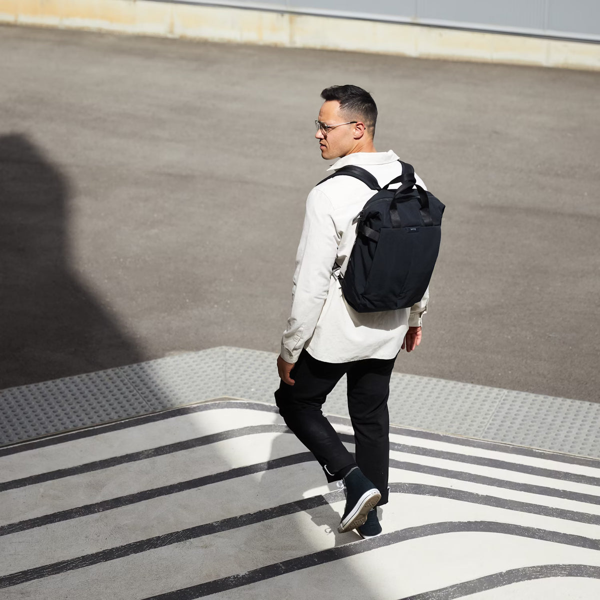 Man walking on a sidewalk with a black Bellroy Totepack backpack
