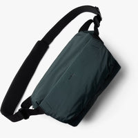 Green sling bag with black strap on a white background