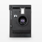 A white Lomography Lomo'Instant Instant Film Camera with a visible lens and flash on a white background.