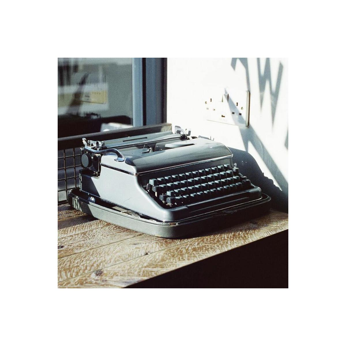 Vintage grey typewriter sitting on a wooden desk in bright daylight, captured on Candido 200 ISO 35mm color film.