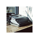 Vintage grey typewriter sitting on a wooden desk in bright daylight, captured on Candido 200 ISO 35mm color film.