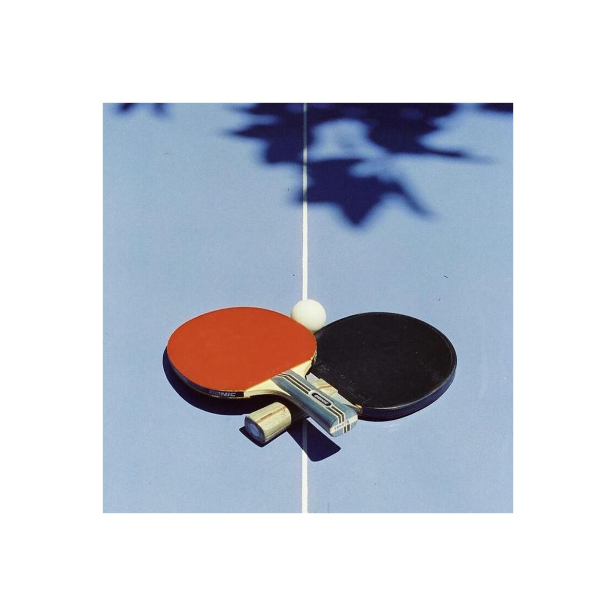 Red and black table tennis paddles with a white ball on a blue table, captured with vivid color and sharp detail.