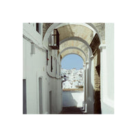 Bright, vivid daylight shot of a white Mediterranean village viewed through a stone archway, captured on 35mm color film.