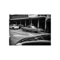Black and white street scene featuring a classic car parked on a city street, captured with fine-grain 120 film.