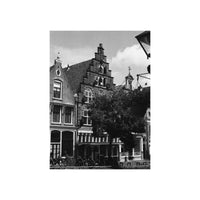 A black and white photograph print depicting traditional European townhouses with gabled roofs, bicycles parked along the street, and a tree in the foreground.