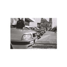Black and white photograph print featuring a row of parked cars in front of a historic church, with a person standing on the hood of the nearest car.