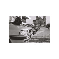 Black and white photograph print featuring a row of parked cars in front of a historic church, with a person standing on the hood of the nearest car.