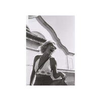 A black and white fashion photograph of a woman laughing and wearing sunglasses, styled with a crochet halter top and dark bottoms, set against an architectural background. The photo is presented as a vertical art print centered on a white canvas.