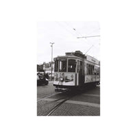 A black and white photograph of a vintage tram on a cobblestone street, presented as a vertical art print centered on a white background.