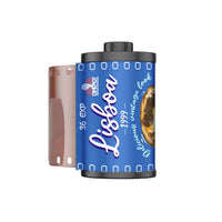 A roll of film with a blue label reading 'Lisboa 1999' and '36 exp', shown on a plain white background. The film has a dark gray/black top and bottom edge, and a translucent pinkish-brown film strip is visible on the left.