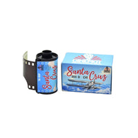 A roll of Santa Cruz 35 mm film next to its blue packaging box, featuring a vintage biplane graphic and the CineMot brand logo, on a plain white background.