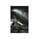A vertical photographic print of a vintage silver airplane nose and propeller inside an aircraft hangar, centered on a white background.