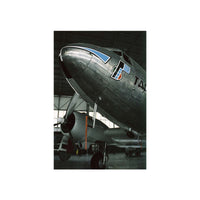 A vertical photographic print of a vintage silver airplane nose and propeller inside an aircraft hangar, centered on a white background.