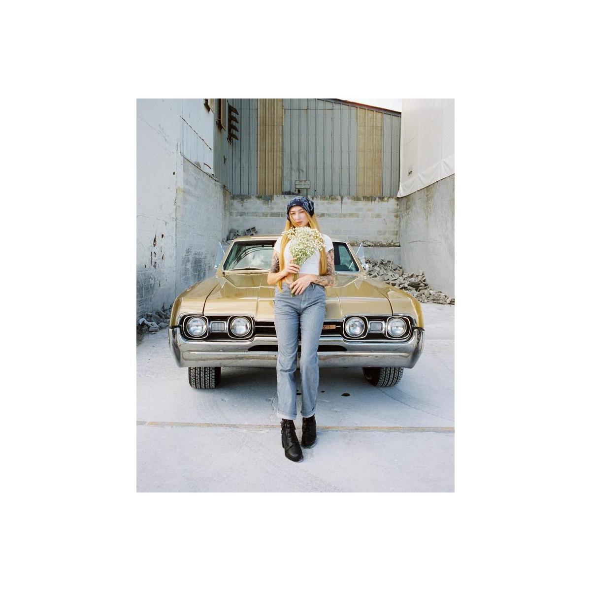 Woman holding flowers standing in front of a vintage gold car, captured on CineStill 400Dynamic 120 film with warm tones.