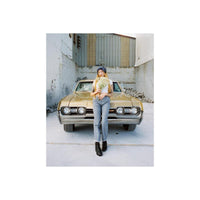 Woman holding flowers standing in front of a vintage gold car, captured on CineStill 400Dynamic 120 film with warm tones.