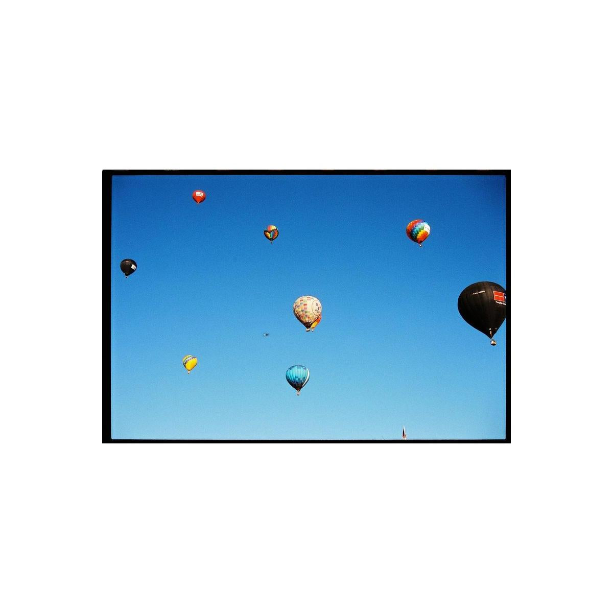 Colorful hot air balloons floating in a clear blue sky, captured on 120 medium format film with a distinct film grain.