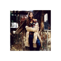 Woman in a plaid top and tan coat leaning against a rustic wooden shed, captured on CineStill 50Daylight 120 film.