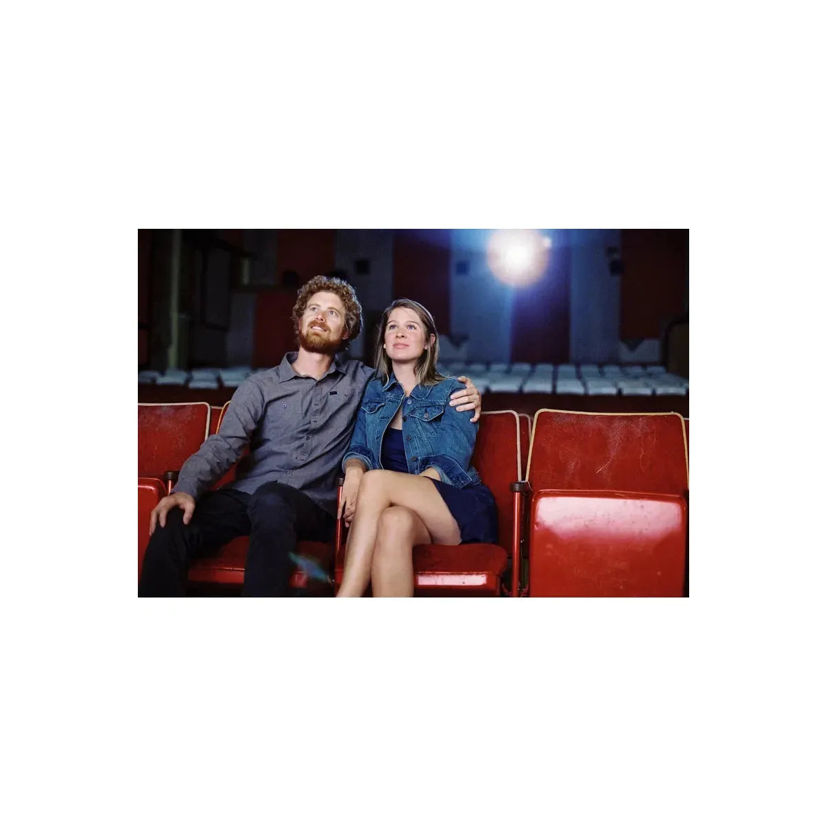 Couple sitting in red vintage theater seats, illuminated by a cinematic light glow, captured on CineStill 800T film.