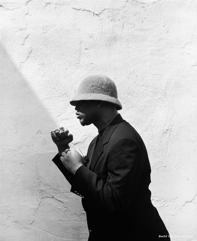 Person wearing a hat and coat against a textured white wall