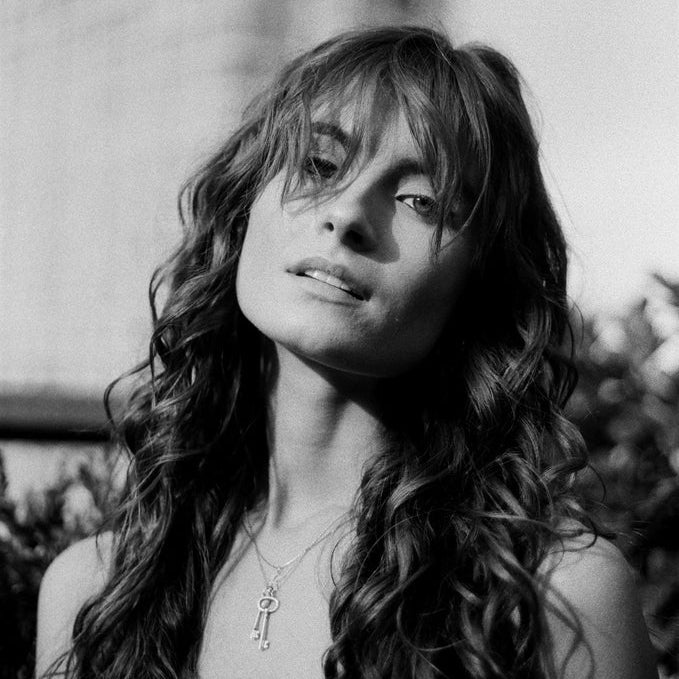 Black and white portrait of a woman with long hair and a key necklace.
