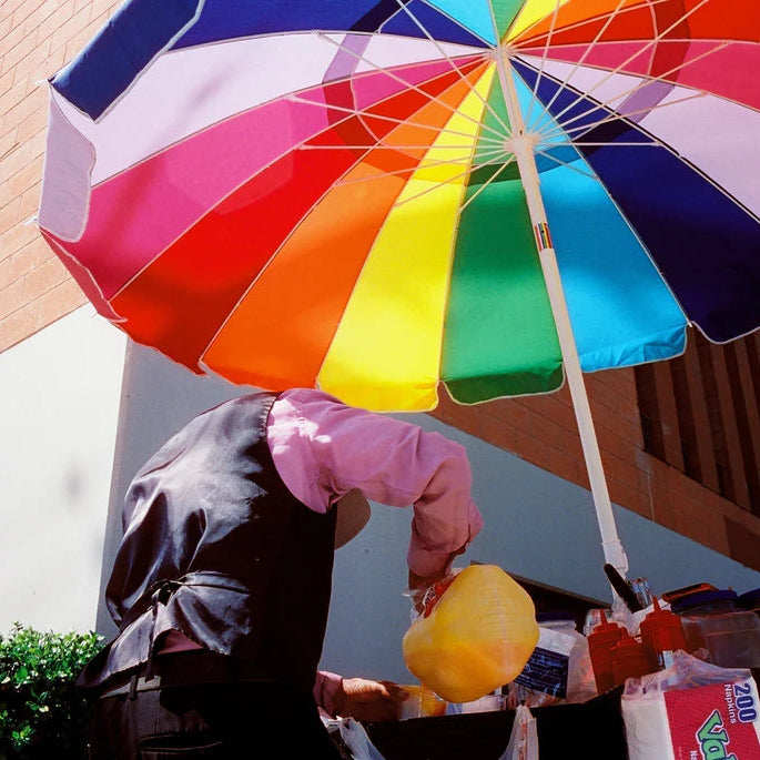 Person holding a colorful umbrella with a market stall in the background