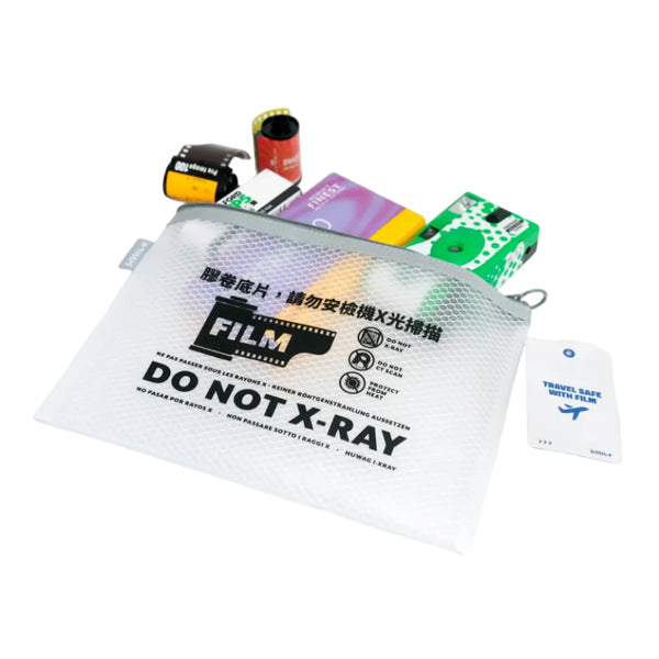 A clear X-ray opaque film pouch with a gray zipper and printed black text reading 'FILM DO NOT X-RAY' on a white background, with sample film reels and colorful inserts placed behind it.